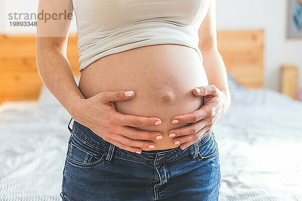 Kaukasische schwangere Mutter  die ihren nackten Bauch berührt  Blue Jeans  Nahaufnahme