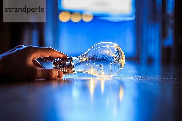 Die Hände halten eine LEDglühbirne über dem Holzboden. Symbol für Ideen und Innovation. Fenster und Licht im unscharfen Hintergrund