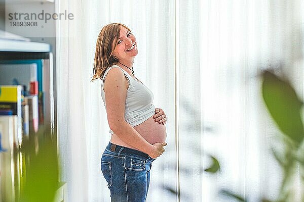 Glückliche kaukasische schwangere Mutter  die ihren nackten Bauch berührt  Blue Jeans  Nahaufnahme