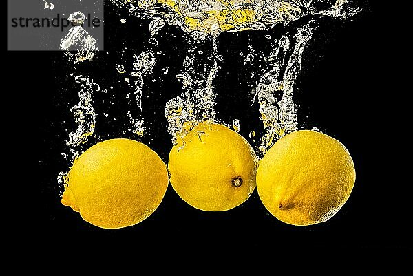 Frische gelbe Zitronen in Wasser spritzen auf schwarzem Hintergrund mit vielen Luftblasen. Erfrischung Konzept