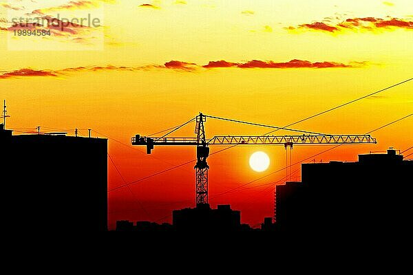 Silhouetten von Häusern und Baukran gegen die untergehende Sonne  Skyline der Stadt bei Sonnenuntergang