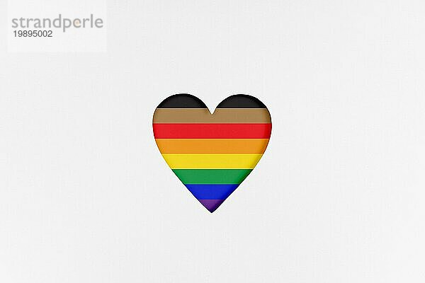 Herzform mit neu gestalteter LGBTQ Stolzflagge auf weißem Karton. Bedruckter Karton mit ausgestanzter Herzform. Ansicht von oben