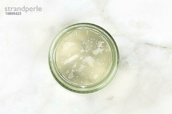 Ein Glasgefäß mit Aloe Vera Gel  aufgenommen von oben auf einem weißen Marmorhintergrund mit Kopierraum