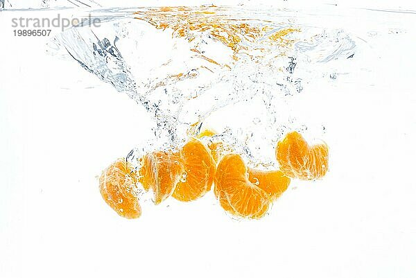 Isolierte fallende Orangensegmente ins Wasser. Geschälte Orangenstücke im Wasser  vor weißem Hintergrund. Gesundheit Konzept