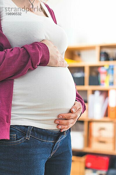 Nahaufnahme eines schwangeren Bauches  kaukasische Mutter mit weißem Hemd und magentafarbener Jacke