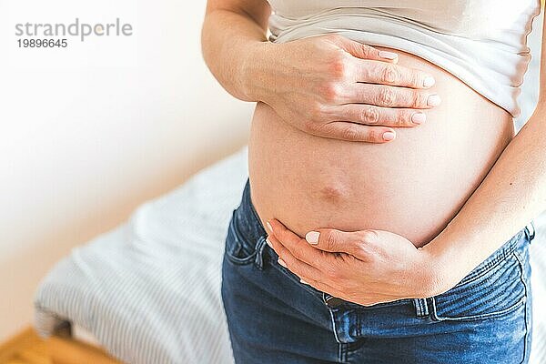 Kaukasische schwangere Mutter  die ihren nackten Bauch berührt  Blue Jeans  Nahaufnahme