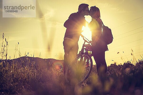 Junges Paar mit Fahrrad küsst sich auf einem Feld  Sonnenuntergang