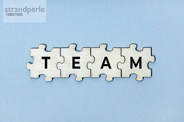 Teamwort auf hölzernen Puzzleteilen vorblauem Hintergrund. Ansicht von oben