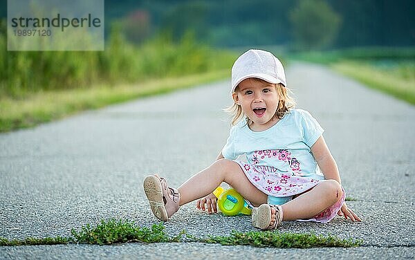 Baby sitzt auf einer asphaltierten Straße zwischen ländlichen landwirtschaftlichen Feldern. Kinder im Freien Konzept