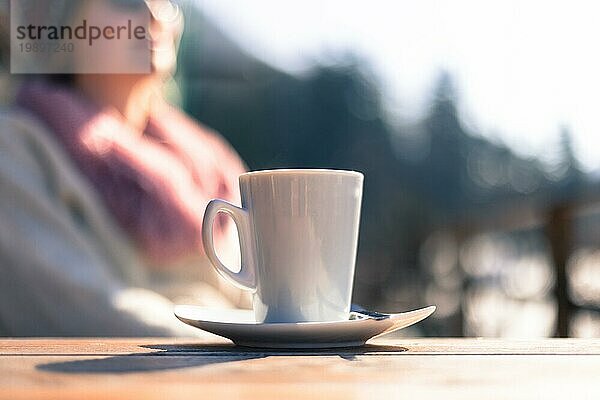 Tasse Kaffee  mit einer Frau im unscharfen Hintergrund. Draußen