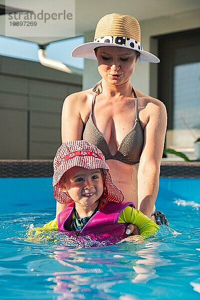 23 Jahre altes Kind mit Mutter im Schwimmbad lernen zu schwimmen. Baby im Schwimmen Westen und roten Hut.Sommer zu Hause Konzept