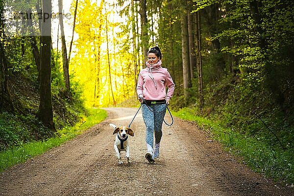 Junge Frau und Hund laufen zusammen im sonnigen Wald. Fröhliche Frau  die mit ihrem Haustier im Freien trainiert. Aktive Menschen Konzept
