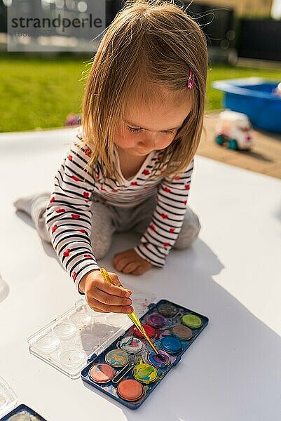 Focused Kind mit Mutter Malerei mit Plakatfarbe im Freien auf dem Boden auf großen Blatt Papier. Kreative Zeit verbringen mit Kindern Konzept