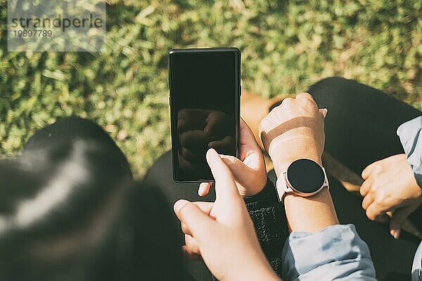 Blick auf die Hand  die den Bildschirm eines Smartphones und einer Smartwatch berührt  drei Personen  die Informationen über soziale Medien auf intelligenten mobilen Geräten austauschen  natürlicher grüner Hintergrund  unscharf