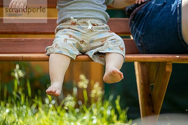 Baby aufwachsen Konzept: Close up von barfuß Baby Füße sitzen auf Parkbank  Sommerzeit