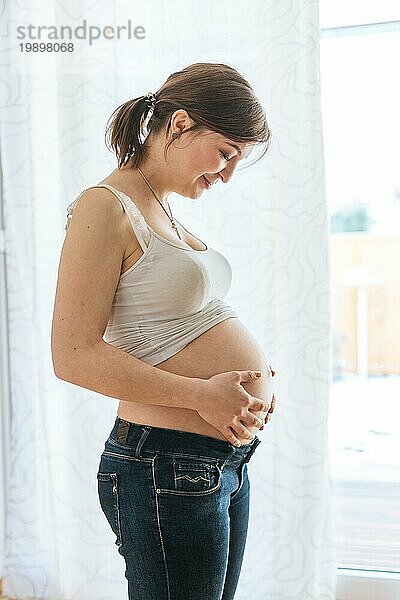 Glückliche kaukasische schwangere Mutter  die ihren nackten Bauch berührt  Blue Jeans  Nahaufnahme