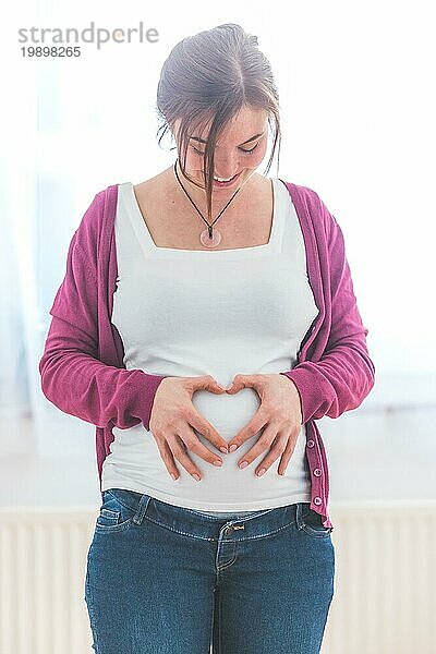 Nahaufnahme des schwangeren Bauches  die Mutter formt ein Herz mit ihren Händen