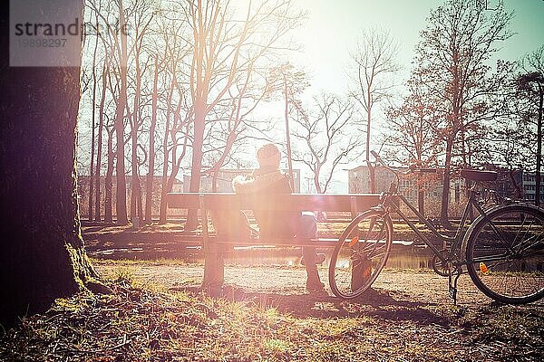 Rückenansicht einer jungen Frau mit Fahrrad  die die Sonne auf einer Parkbank genießt  Frühling