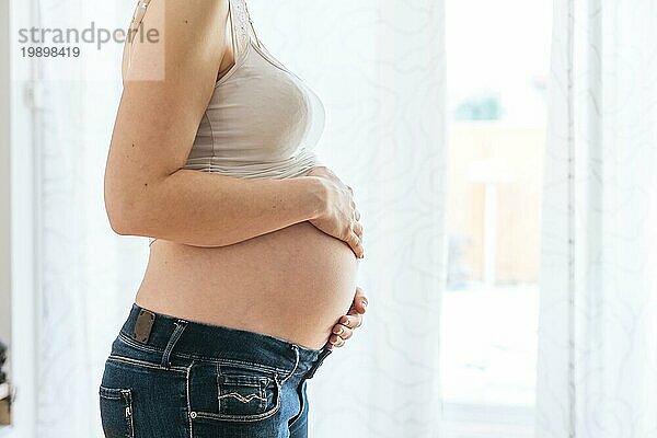 Glückliche kaukasische schwangere Mutter  die ihren nackten Bauch berührt  Blue Jeans  Nahaufnahme