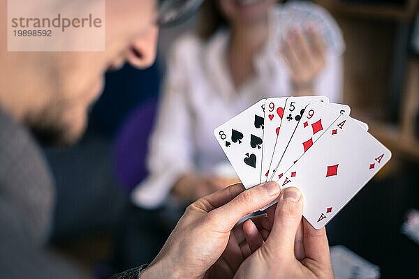 Kartenspielen zu Hause: Freunde sitzen an einem Tisch. Mann spielt Karten  Mann im unscharfen Hintergrund