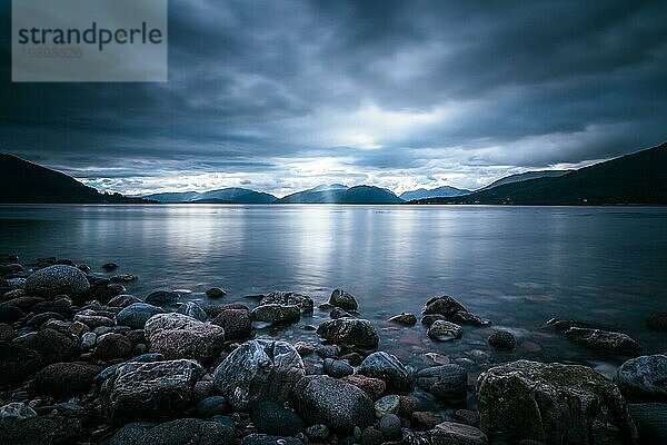 Schöne mystische Landschaft Seelandschaft in Schottland mit bewölktem Himmel und Sonnenstrahlen