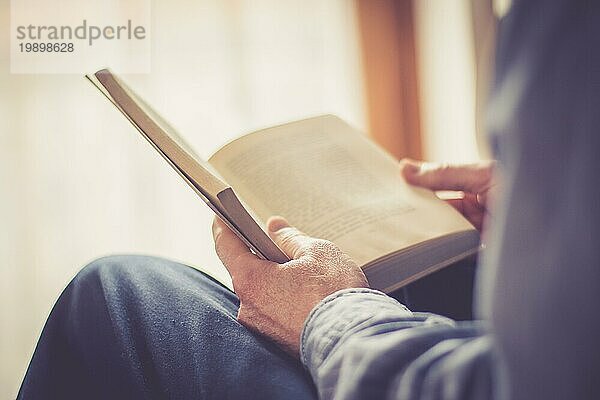 Ausgeschnittenes Bild eines älteren Mannes  der zu Hause ein Buch liest