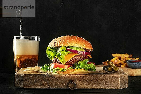 Burger und Bier. Hamburger mit Rindfleisch  Käse  Zwiebeln  Tomaten und grünem Salat  eine Seitenansicht auf einem dunklen Hintergrund mit Kopierraum  Gurken und Pommes frites. Selektiver Fokus