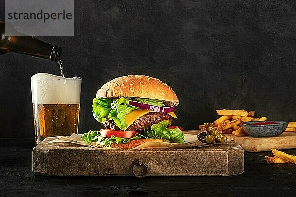 Burger und Bier. Hamburger mit Rindfleisch  Käse  Zwiebel  Tomate und grünem Salat  eine Seitenansicht auf einem dunklen Hintergrund mit Kopierraum  Gewürzgurken  Pommes frites und Ketchup. Selektiver Fokus