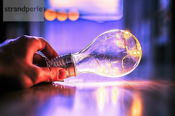 Die Hände halten eine LEDglühbirne über dem Holzboden. Symbol für Ideen und Innovation. Fenster und Licht im unscharfen Hintergrund