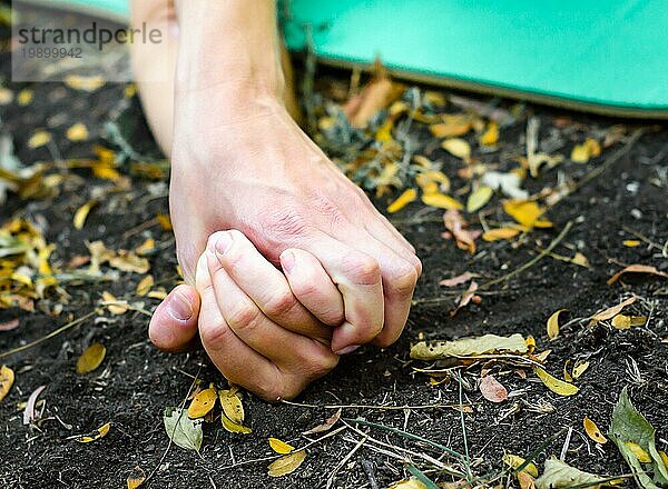 Hände von Menschen  die sich gegenseitig auf dem Boden halten  umgeben von Blättern