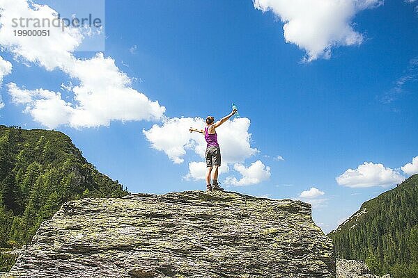 Ziel erreicht: Sportliches Mädchen steht auf einem großen Felsen und hebt die Hände in die Luft