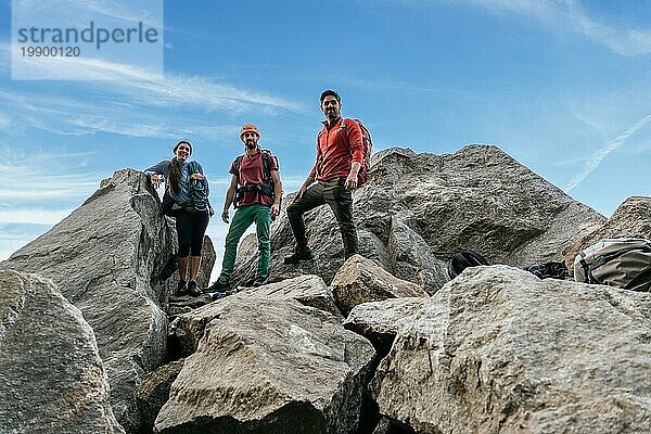 Eine Gruppe von Kletterfreunden  die lächelnd in die Kamera schauen  wenn sie oben am Felsen stehen. Gemischtes Team beim Klettern
