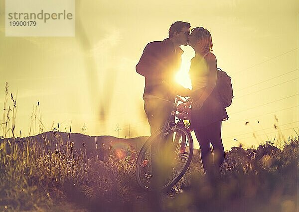 Junges Paar mit Fahrrad küsst sich auf einem Feld  Sonnenuntergang