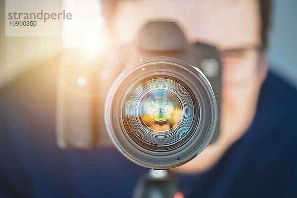 Der Fotograf steht hinter einer professionellen Kamera mit Teleobjektiv auf einem Stativ. Sonnenstrahl