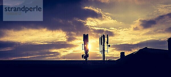 Silhouette eines Fernmelde oder Mobilfunkmastes auf dem Dach eines Gebäudes  Abendsonne