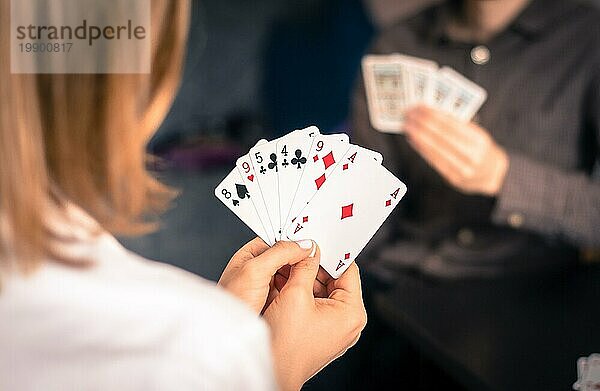 Kartenspielen zu Hause: Freunde sitzen an einem Tisch. Frau spielt Karten  Mann im unscharfen Hintergrund
