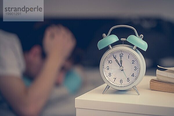 Weißer Wecker auf dem Nachttisch. Junge versucht  im Hintergrund zu schlafen  Schlaflosigkeit