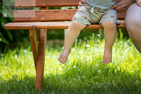 Baby aufwachsen Konzept: Close up von barfuß Baby Füße sitzen auf Parkbank  Sommerzeit