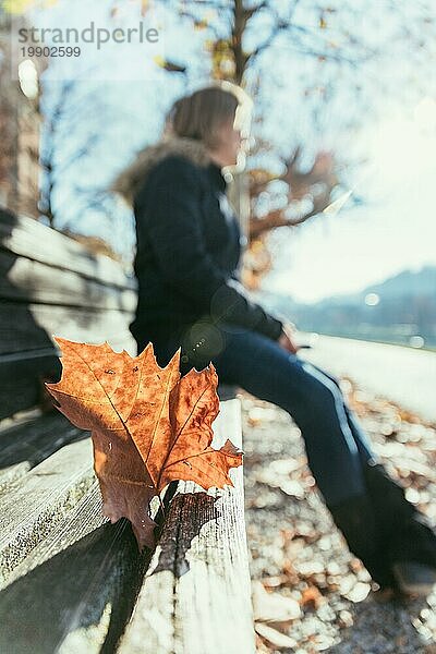 Parkbank im Herbst  darauf sitzende Frau im unscharfen Hintergrund