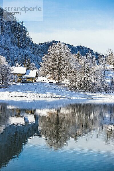 Idyllische Winterlandschaft: Spiegelung See  Haus und verschneite Bäume und Berge