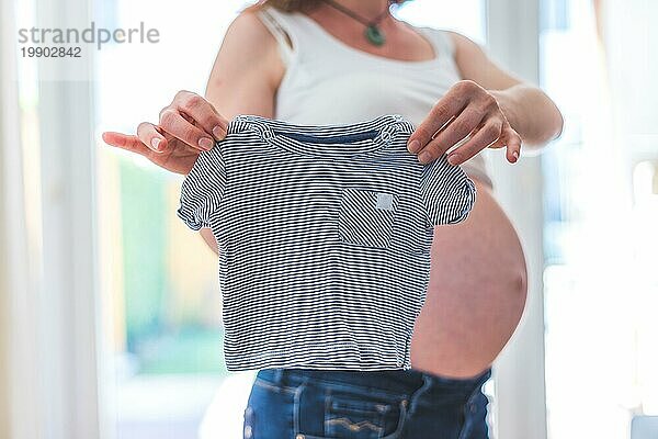 Glückliche kaukasische schwangere Mutter mit kleinem Baby Shirt