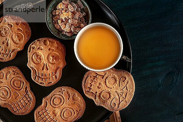 Halloween Ingwerplätzchen in Form von Totenköpfen  hausgemachte Dia de los muertos Kekse  Aufnahme von oben mit Kopierbereich auf dunklem Holzhintergrund