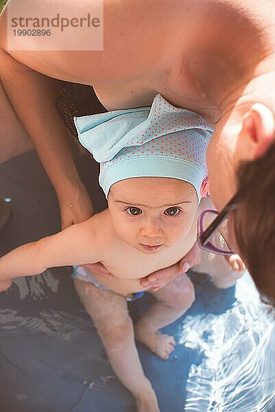 Mutter hält ihr kleines Mädchen zum ersten Mal im Schwimmbad. Sommeraktivitäten