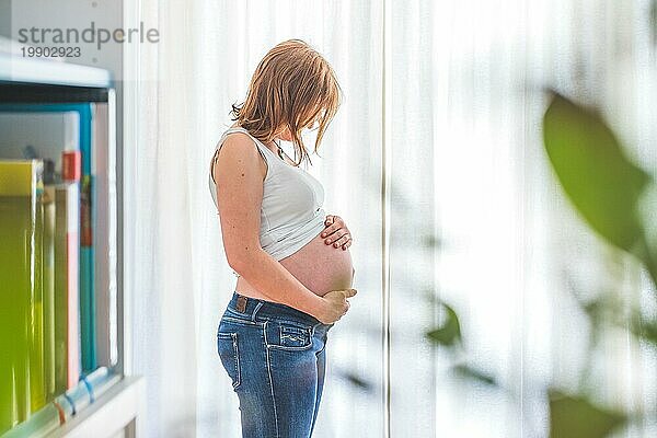 Glückliche kaukasische schwangere Mutter  die ihren nackten Bauch berührt  Blue Jeans  Nahaufnahme