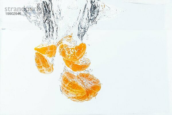 Isolierte fallende Orangensegmente ins Wasser. Geschälte Orangenstücke im Wasser  vor weißem Hintergrund. Gesundheit Konzept