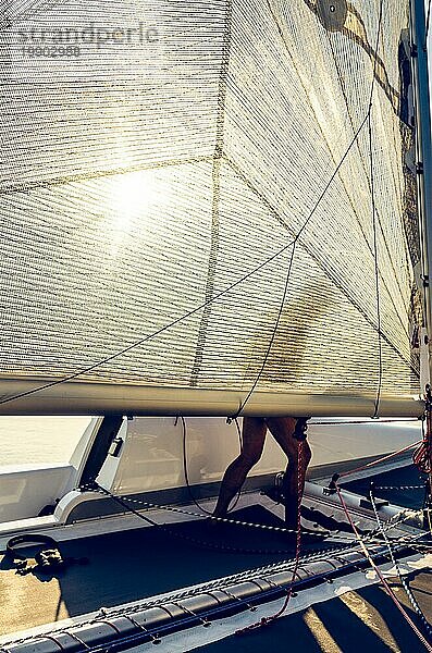 Mann auf einem Katamaranboot hinter Segel. Hintergrundbeleuchtete Sommererholung