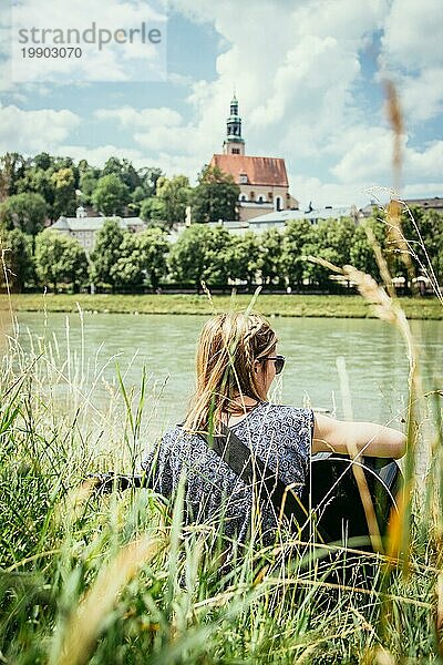 Schönes junges Mädchen sitzt an einem Fluss und spielt ihre Westerngitarre