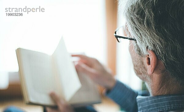 Ausgeschnittenes Bild eines älteren Mannes  der zu Hause ein Buch liest