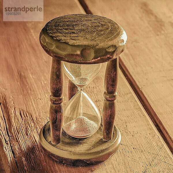 Zeit Konzept. Ein Vintage Sanduhr mit Sand fallen durch  auf einem rustikalen Hintergrund  getönten quadratisches Bild