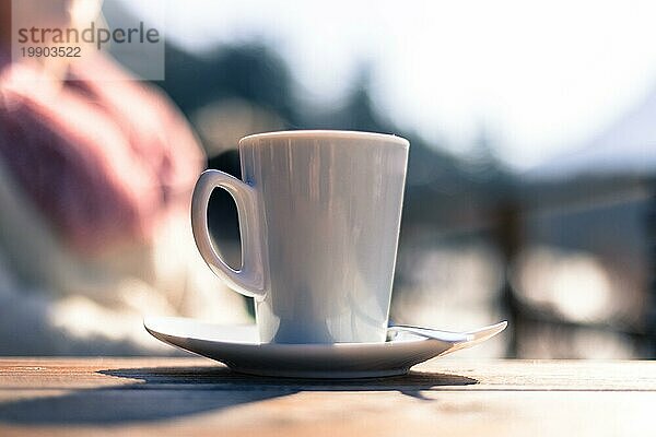 Tasse Kaffee  mit einer Frau im unscharfen Hintergrund. Draußen